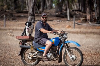 Photo of Roger on a motorbike on the farm, with the farm dog.