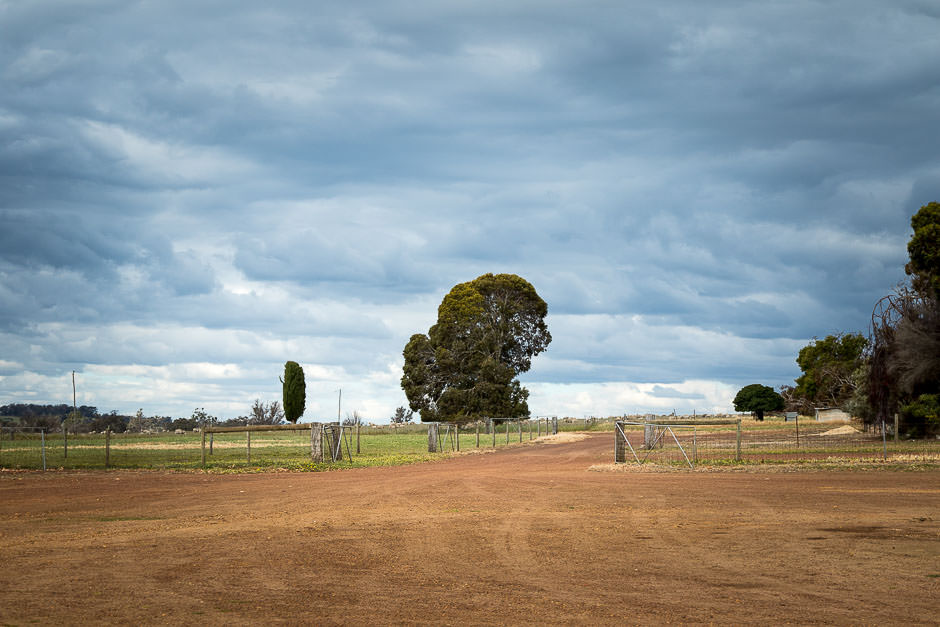photo of grey cloudy sky over farmland with farm driveway and gates
